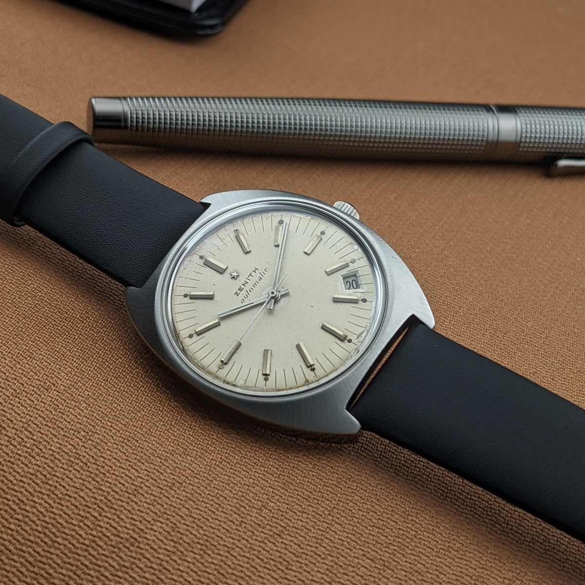 Angled view of the Zenith Automatic reference GR 720001 with light dial, date window, black strap, and textured silver pen.
