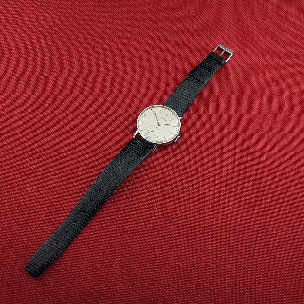Longines Calatrava reference 20757 pictured diagonally across red fabric, showing the complete black strap, buckle, and light dial.