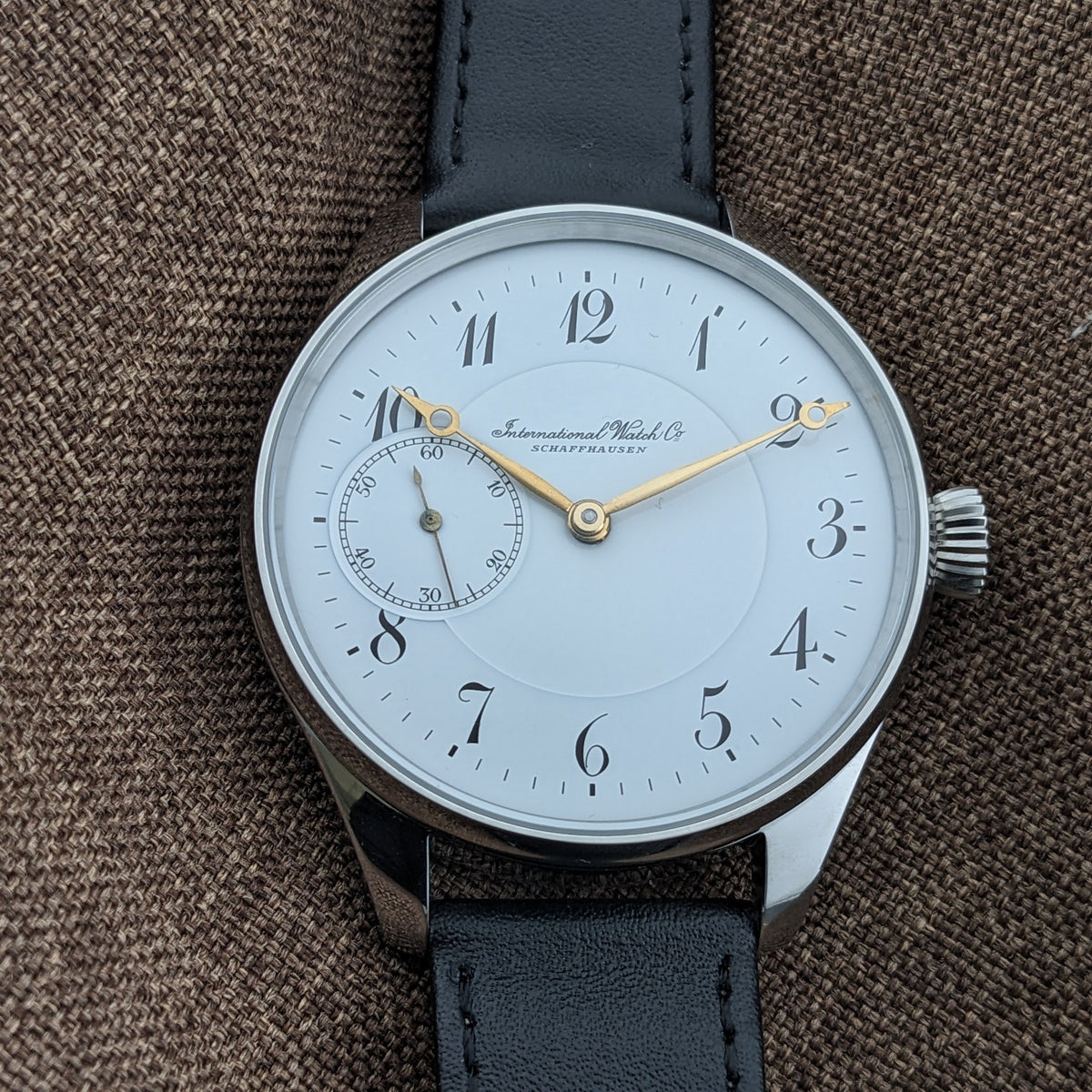 IWC Schaffhausen डायल का सीधा दृश्य, 12-घंटे का लेआउट, सुनहरे हाथ, काले अरबी अंक और बाईं ओर छोटे सेकंड्स रजिस्टर दिखाता हुआ।