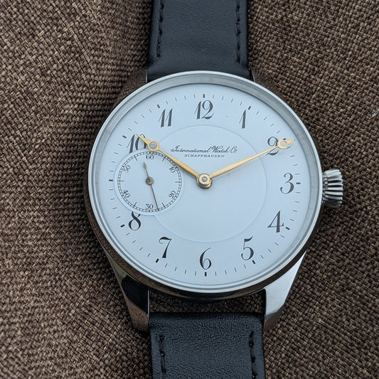 IWC Schaffhausen डायल का सीधा दृश्य, 12-घंटे का लेआउट, सुनहरे हाथ, काले अरबी अंक और बाईं ओर छोटे सेकंड्स रजिस्टर दिखाता हुआ।