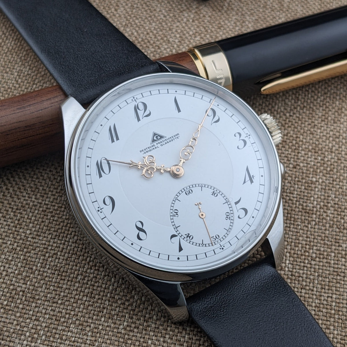 Dreiviertelansicht der Deutsche Präzisionsuhr „Original Glashütte” mit weißem Zifferblatt, schwarzen Ziffern, goldfarbenen Zeigern