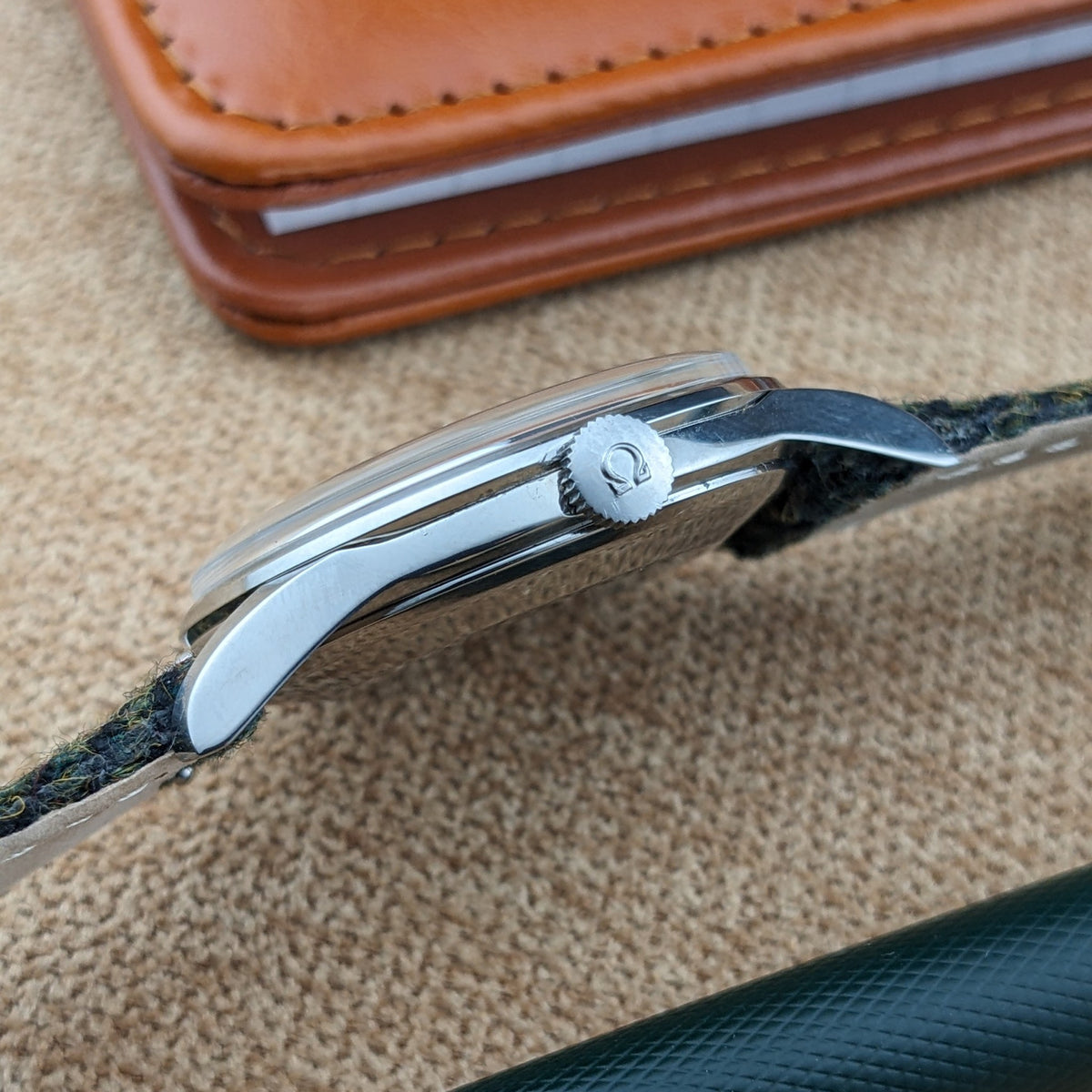 Seitenprofil der Omega Classic Referenz 2810-2 SC zeigt das polierte Gehäuse, Bandanstöße und geriffelte Krone neben einem braunen Notizbuch.