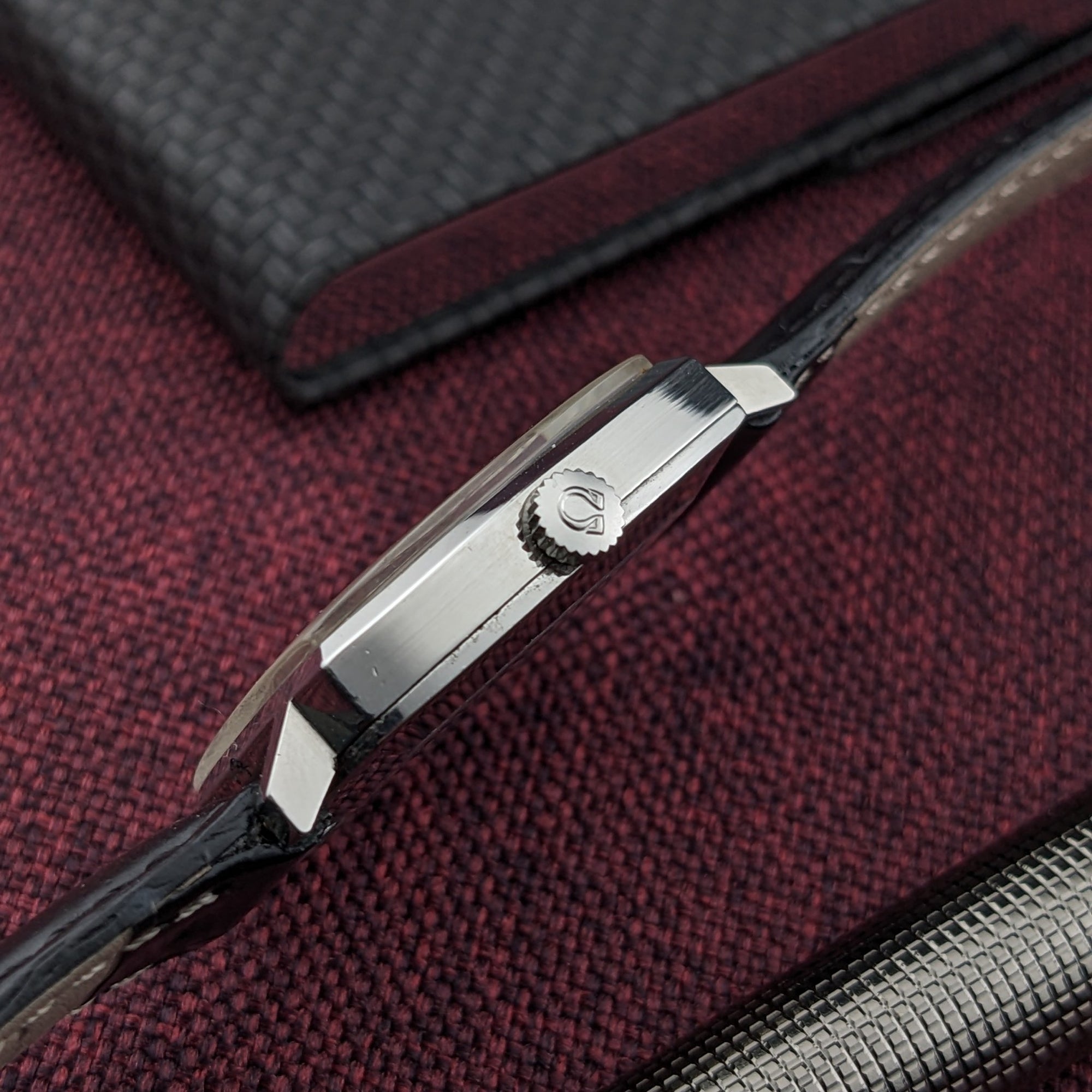 Side profile of the Omega Genève reference 131.022, showing the polished case edge, Omega crown, lugs, and black strap.
