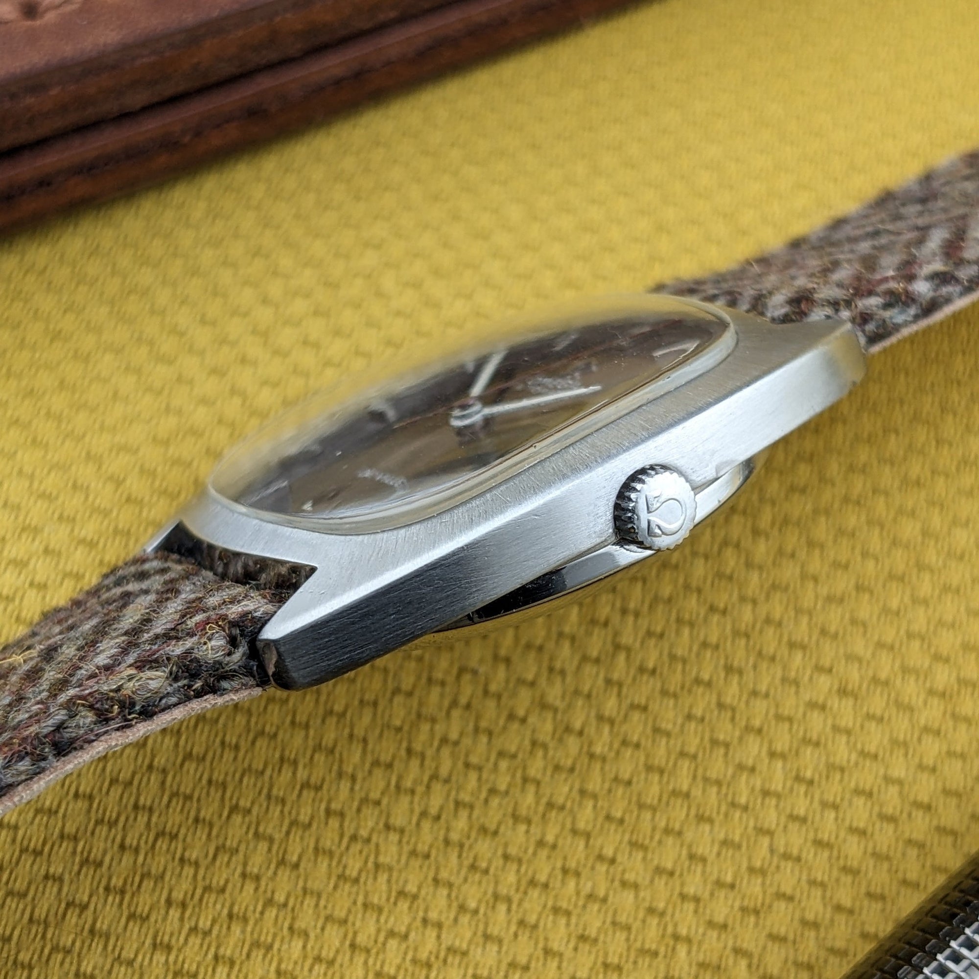 Low side view of the Omega Dr Ville Automatic ref. 162.045, showing the crystal, case flank, Omega-marked crown, and woven strap.