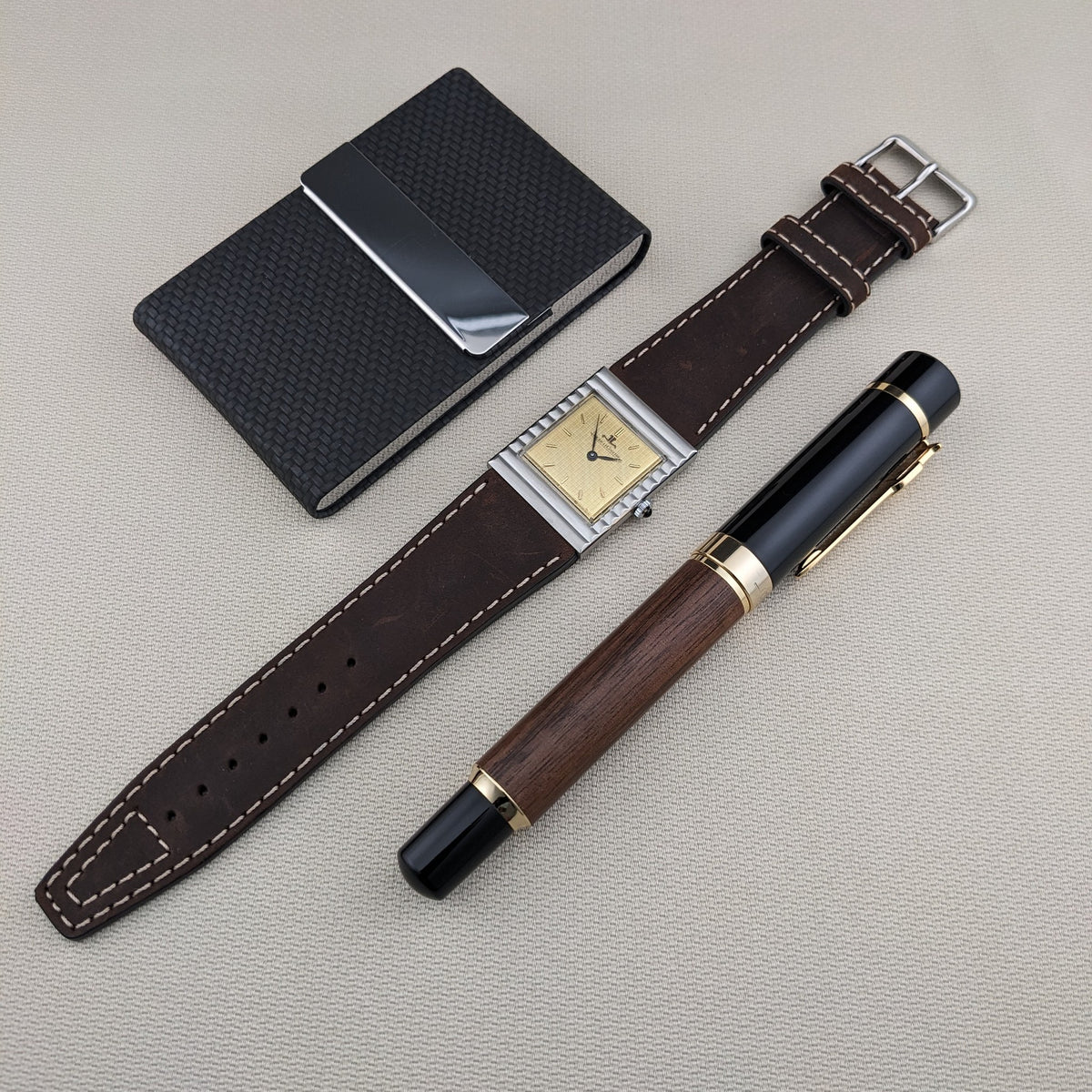 Gesamtansicht der Jaeger-LeCoultre Vogue Tank Ref. 9120 mit ihrem langen braunen Armband, schwarzem Notizbuch und Holz-Schwarz-Stift.