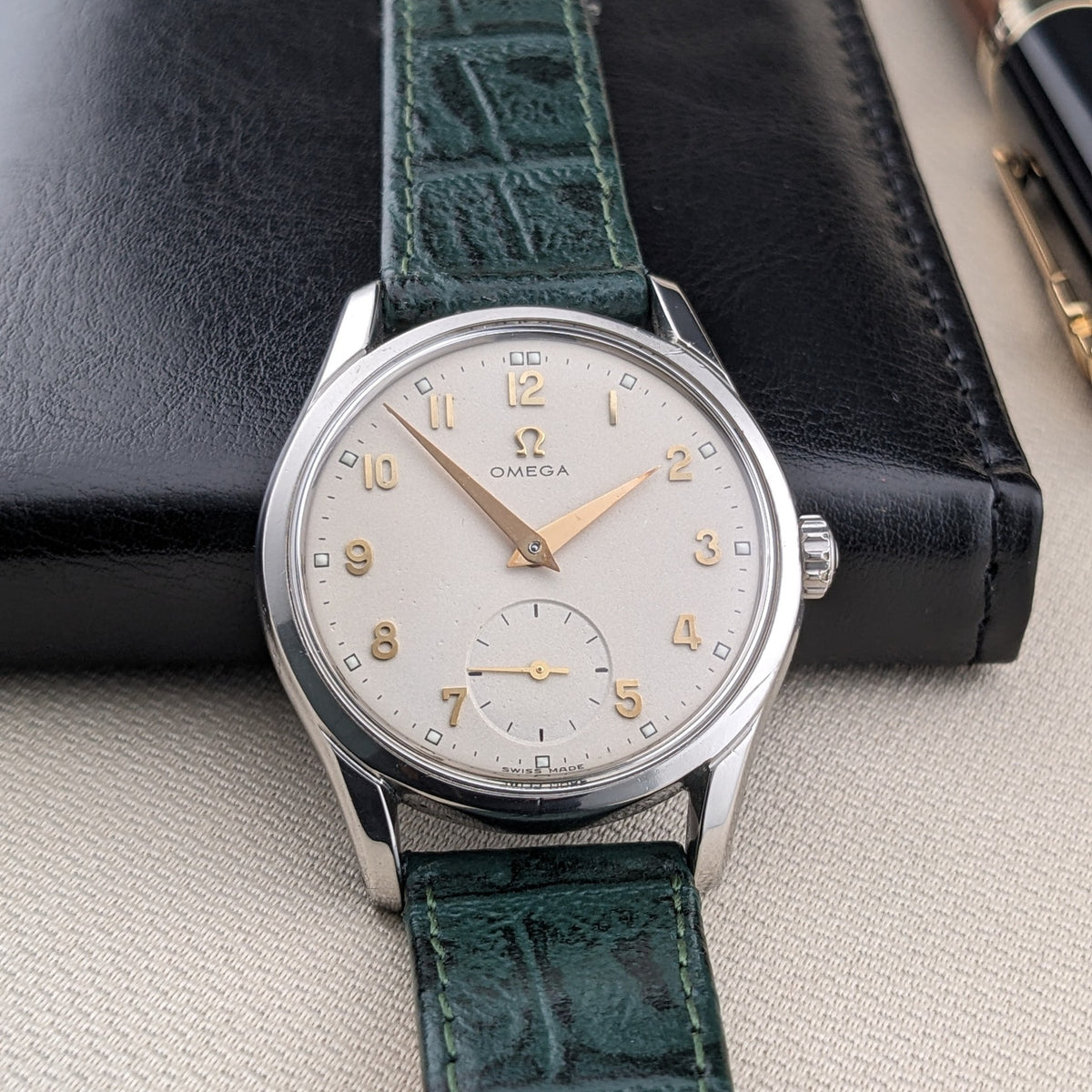 OMEGA Classic 2639-11 frontale con quadrante argentato, numeri arabi dorati, secondi ausiliari, cinturino verde e custodia in pelle nera dietro.