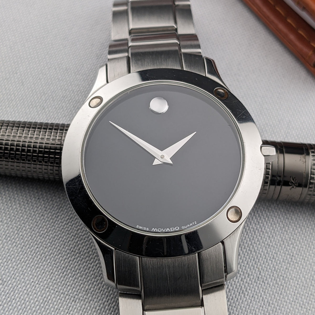 Cadran Movado de face avec aiguilles argentées, repère circulaire, lunette polie, attaches visibles et maillons de bracelet.