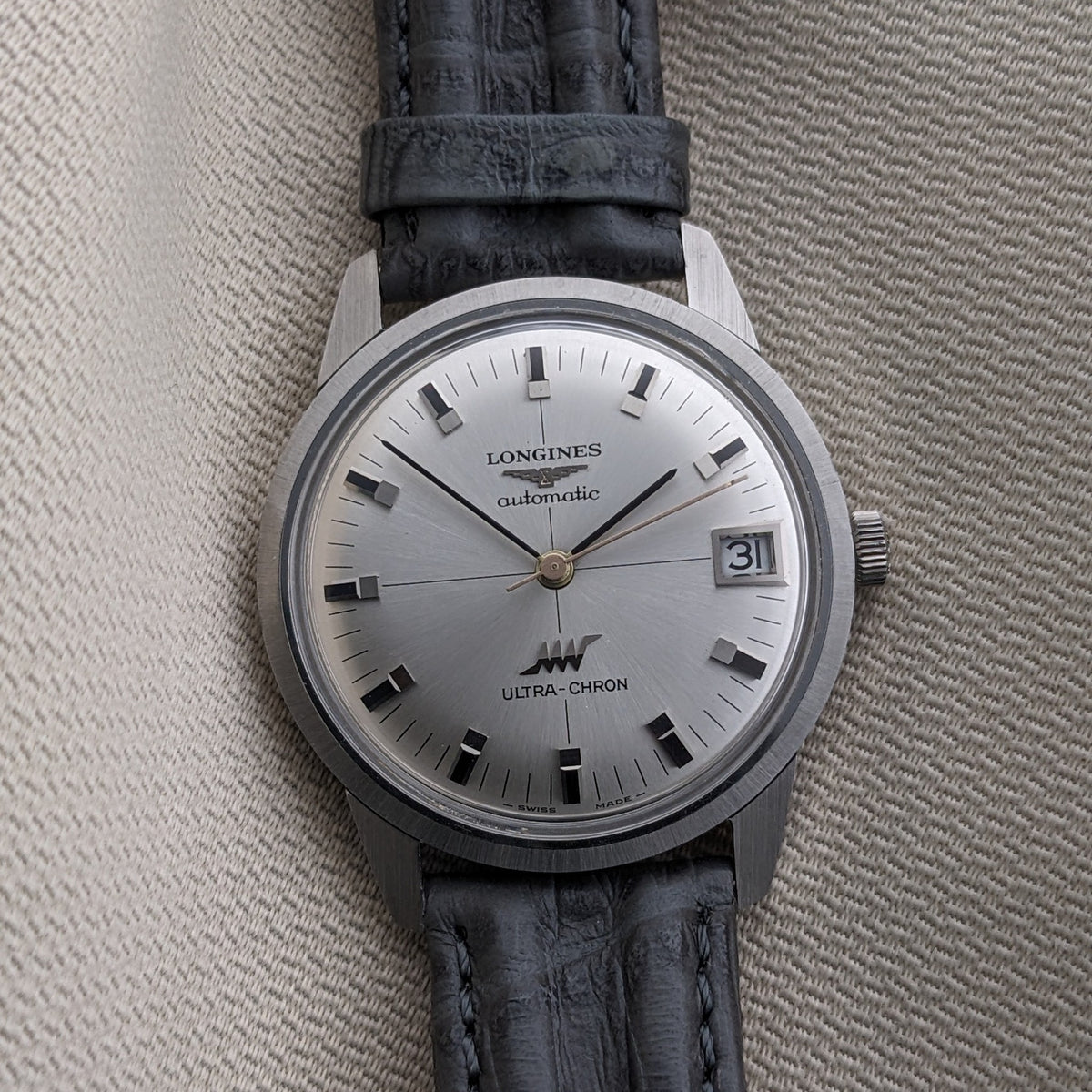 Longines Ultra-Chron 7827 presented vertically on a black leather strap, with silver dial, date window, baton markers, and central hands.