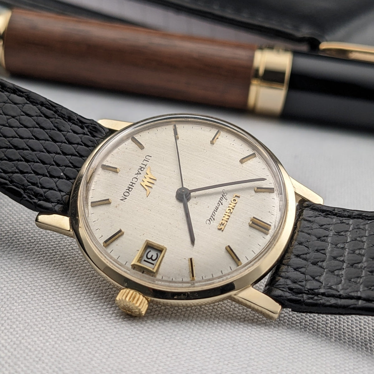 Low angled view of the Longines Ultra-Chron reference 69-556AC showing its cream dial, date window, gold-tone case, crown, and strap.