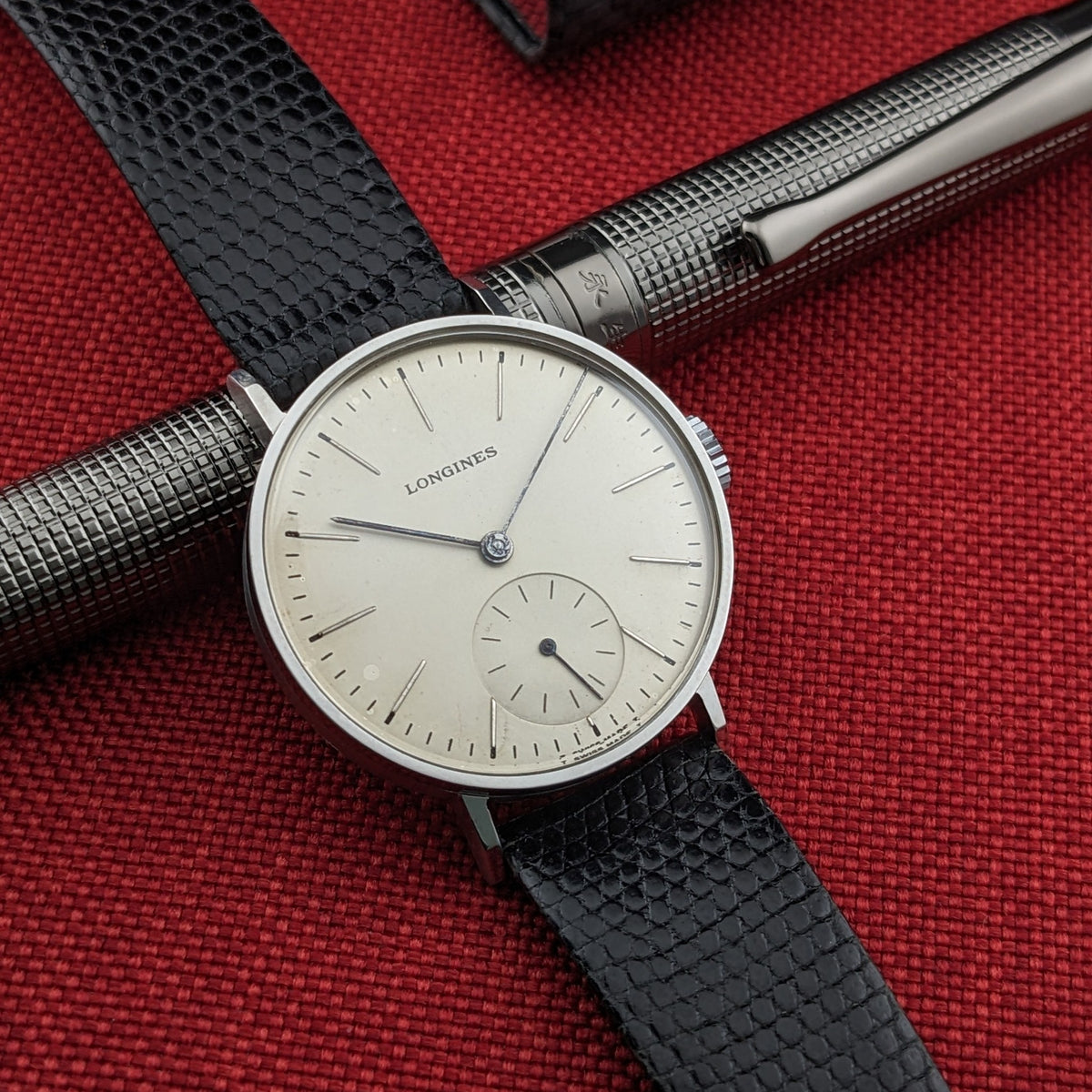 Close angled composition of the Longines Calatrava reference 20757 dial over a silver pen, highlighting the small-seconds subdial and black strap.
