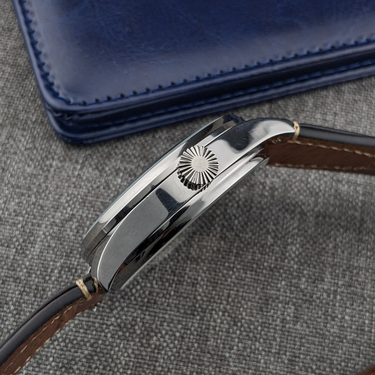 Ulysse Nardin घड़ी क्राउन साइड से देखी गई, जिसमें रिड्ज़ क्राउन, चमकदार केस फ्लैंक, लग्स और चमड़े का पट्टा दिखता है।