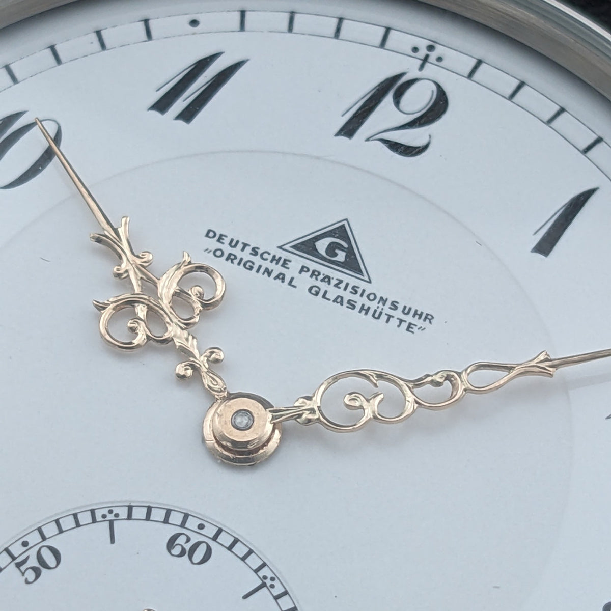 Makrodetail des Zifferblatts der Deutsche Präzisionsuhr „Original Glashütte”, zeigt den gedruckten Namen, Emblem und dekorativ