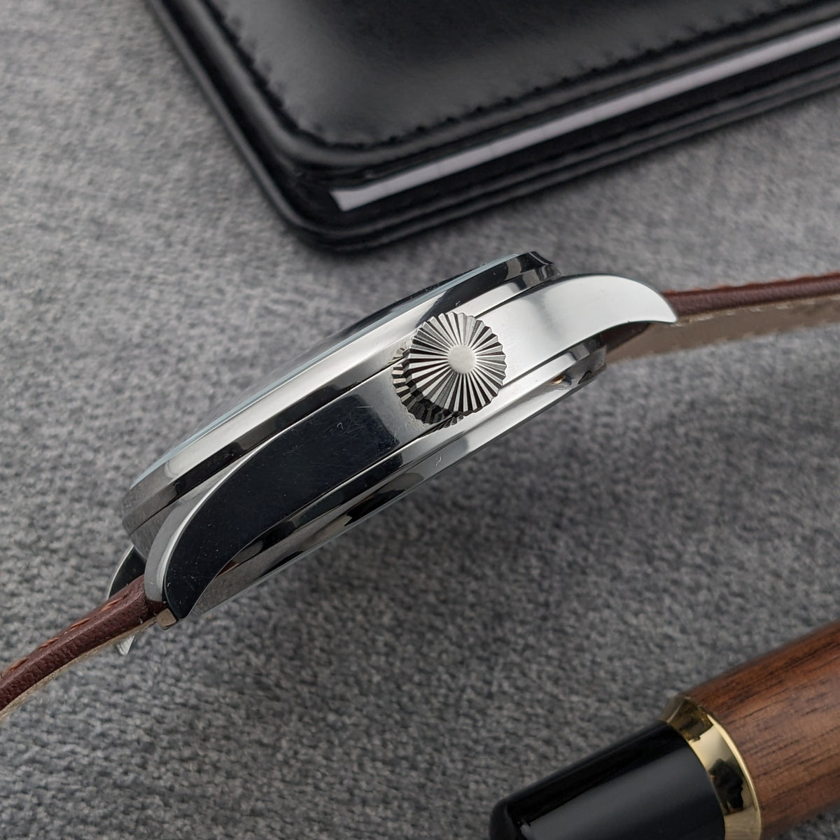 Profilo laterale dell'orologio Omega con bordo della cassa lucido, anse curve, corona zigrinata e cinturino marrone sottile.