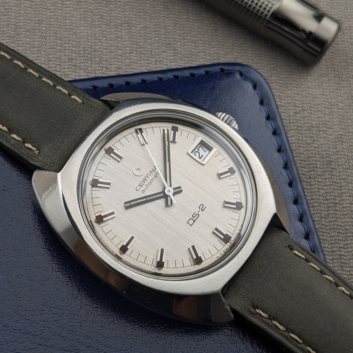 Certina DS-2 Automatic reference 5801 300 laid over a blue wallet, showing the silver dial, date aperture, and contrasting strap stitching.