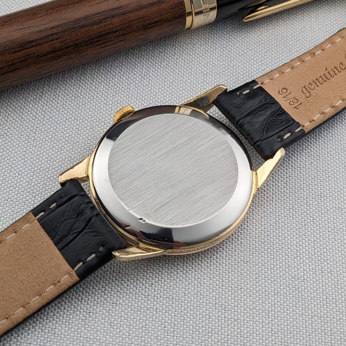 Rear exterior of the Omega Classic reference 14391-1 with a plain circular caseback, black strap and tan strap lining visible.