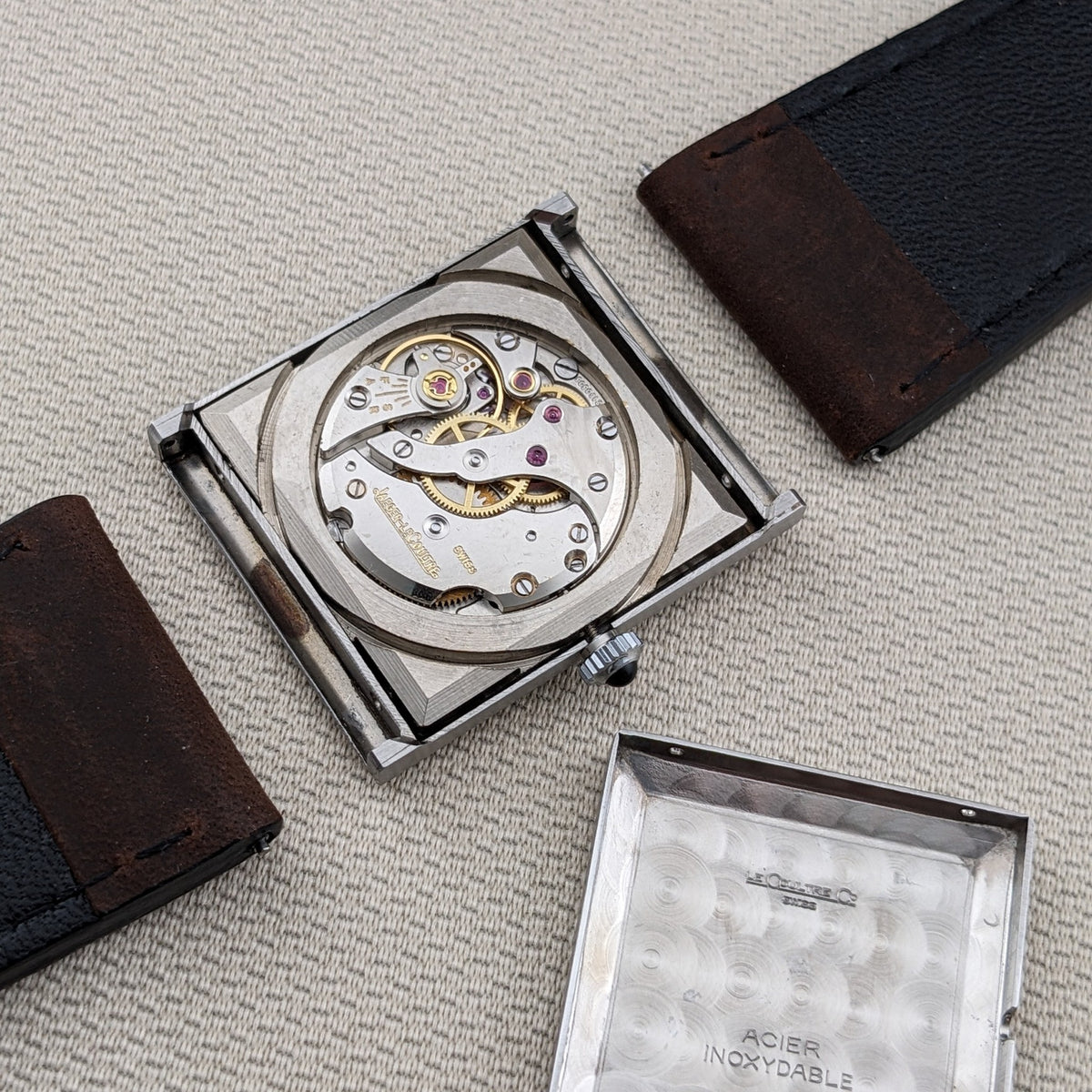 Offene Jaeger-LeCoultre Vogue Tank Ref. 9120 zeigt das sichtbare mechanische Uhrwerk, abgenommenen Gehäuseboden, Krone und braune Armbandenden.