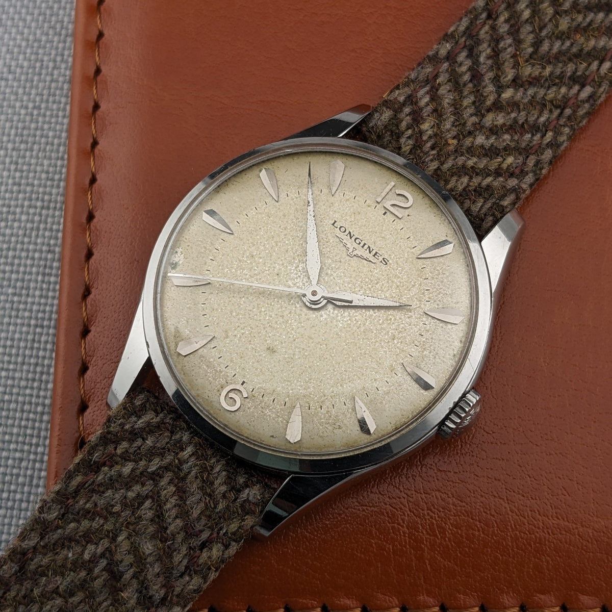 Longines Classic reference 8135-5 displayed diagonally on a tan leather wallet, with the cream dial, silver case and woven strap visible.