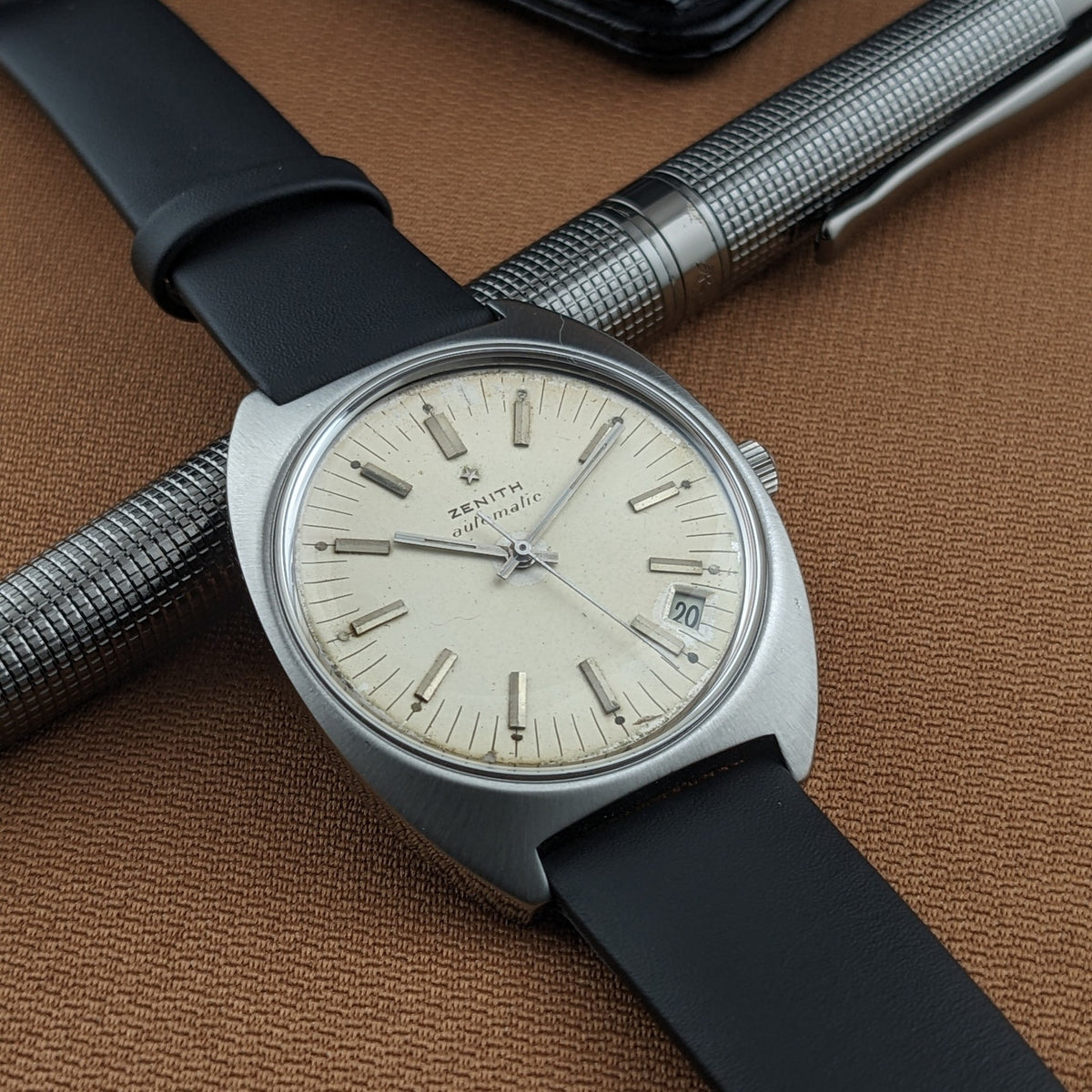 Three-quarter view of the Zenith Automatic reference GR 720001 beside a textured silver pen on brown fabric.
