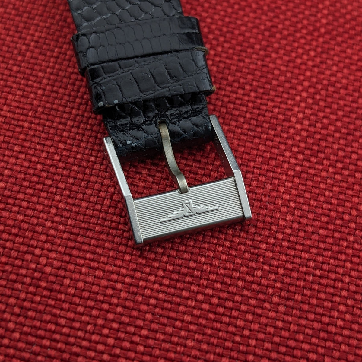Close-up of the Longines Calatrava reference 20757 strap buckle on red fabric, featuring horizontal lines and a raised Longines emblem.