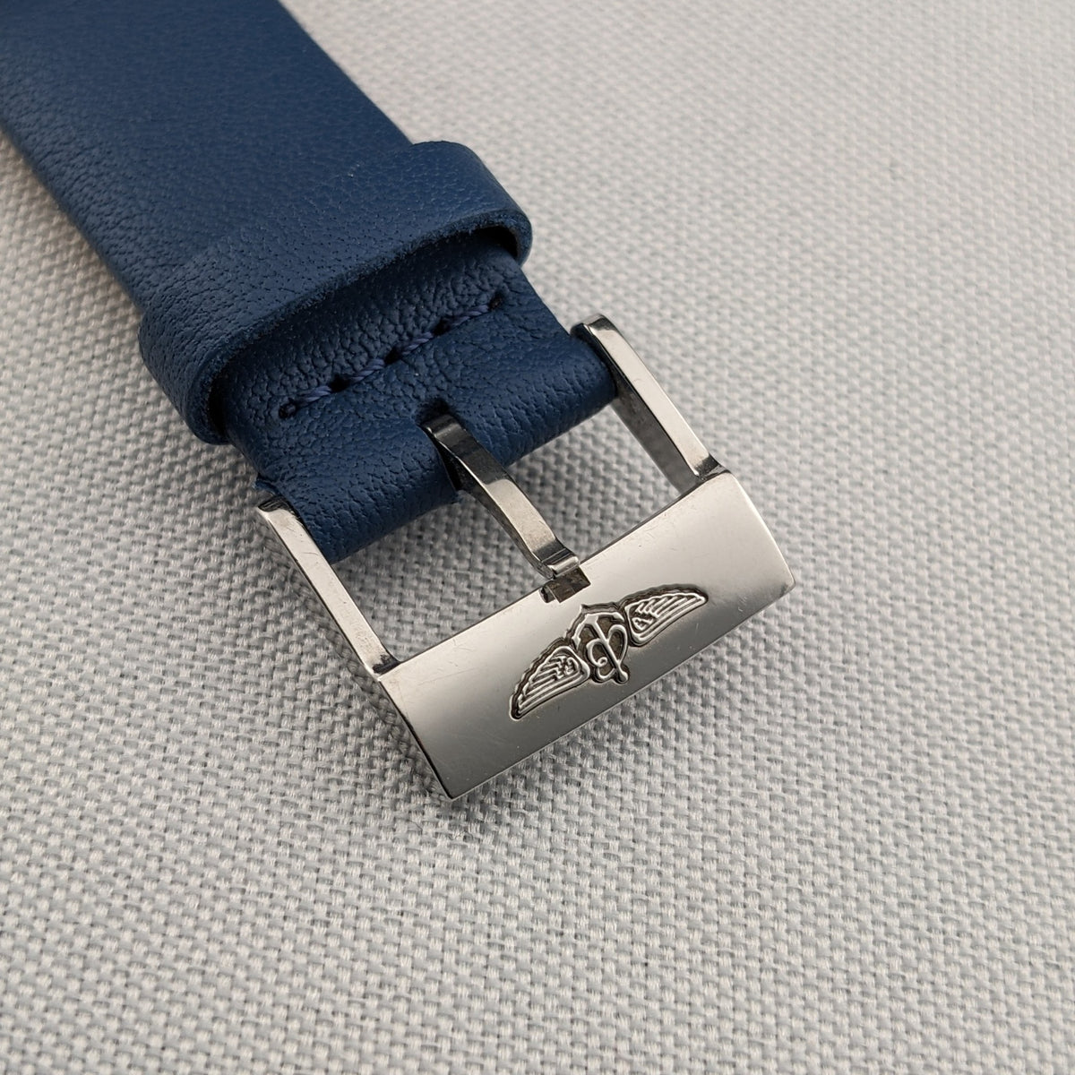 Close-up of the blue Breitling strap and polished buckle, featuring a raised winged Breitling emblem.