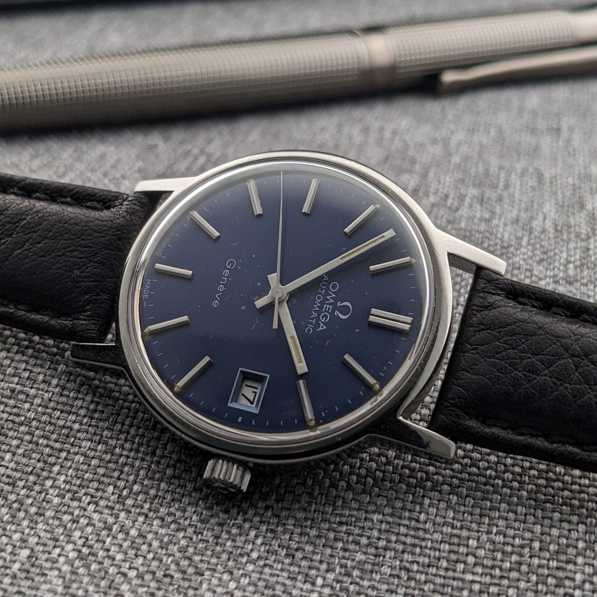 Rotated view of the Omega Geneve Automatic reference 166.0163, showing its blue dial, date window, silver markers and black strap.