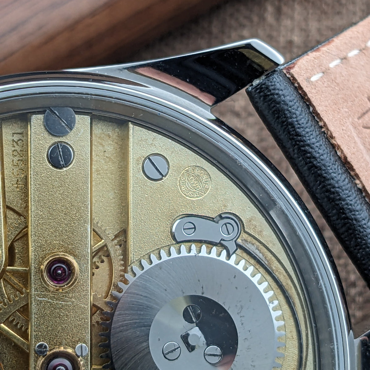 IWC Schaffhausen मूवमेंट का प्रदर्शनी बैक के माध्यम से विस्तृत दृश्य, गिल्ट ब्रिज, बड़े सिल्वर गियर और उत्कीर्ण प्रतीक को दिखाता हुआ।