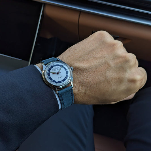 Atlantic Varldsmastarur visible on a wrist inside a vehicle, with the blue strap and watch face framed by dark clothing and interior details.