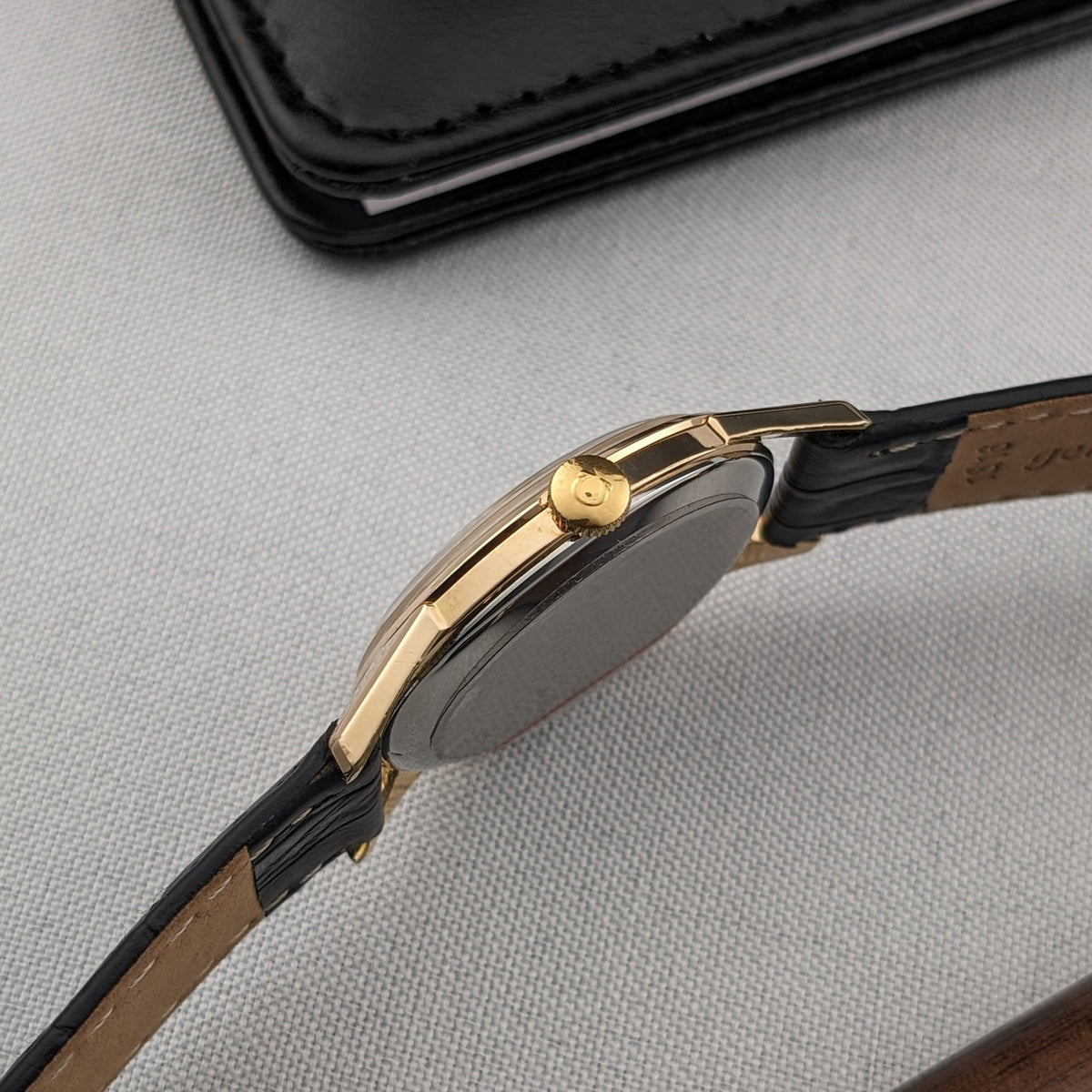 Side profile of the Omega Classic reference 14391-1, showing the slim gold-tone case, crown, lugs and strap edges against gray fabric.