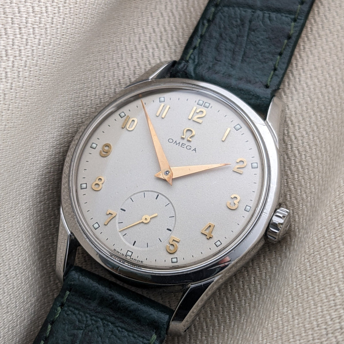 Primo piano angolato del quadrante argentato OMEGA Classic 2639-11 con numeri dorati, secondi ausiliari, cassa lucida e cinturino verde.