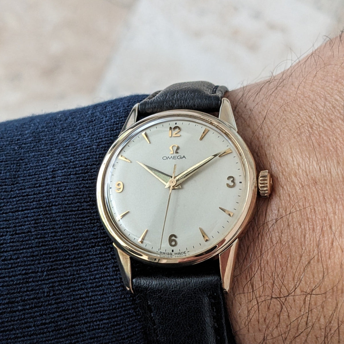 Omega Classic référence 14392-61-SC portée sur un poignet, avec son cadran crème, ses index dorés et son bracelet en cuir noir clairement visibles.