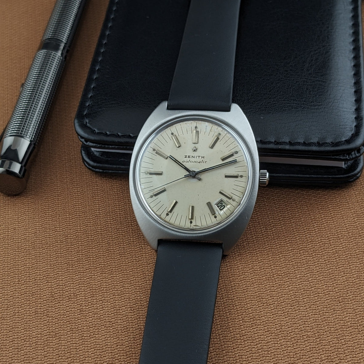 Zenith Automatic reference GR 720001 centered over a black case, with black strap and silver pen visible at the side.