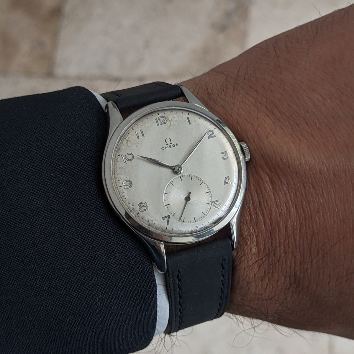 Omega Jumbo reference 2505-5 worn on a wrist beneath a dark sleeve, showing its silver-toned dial and black leather strap.