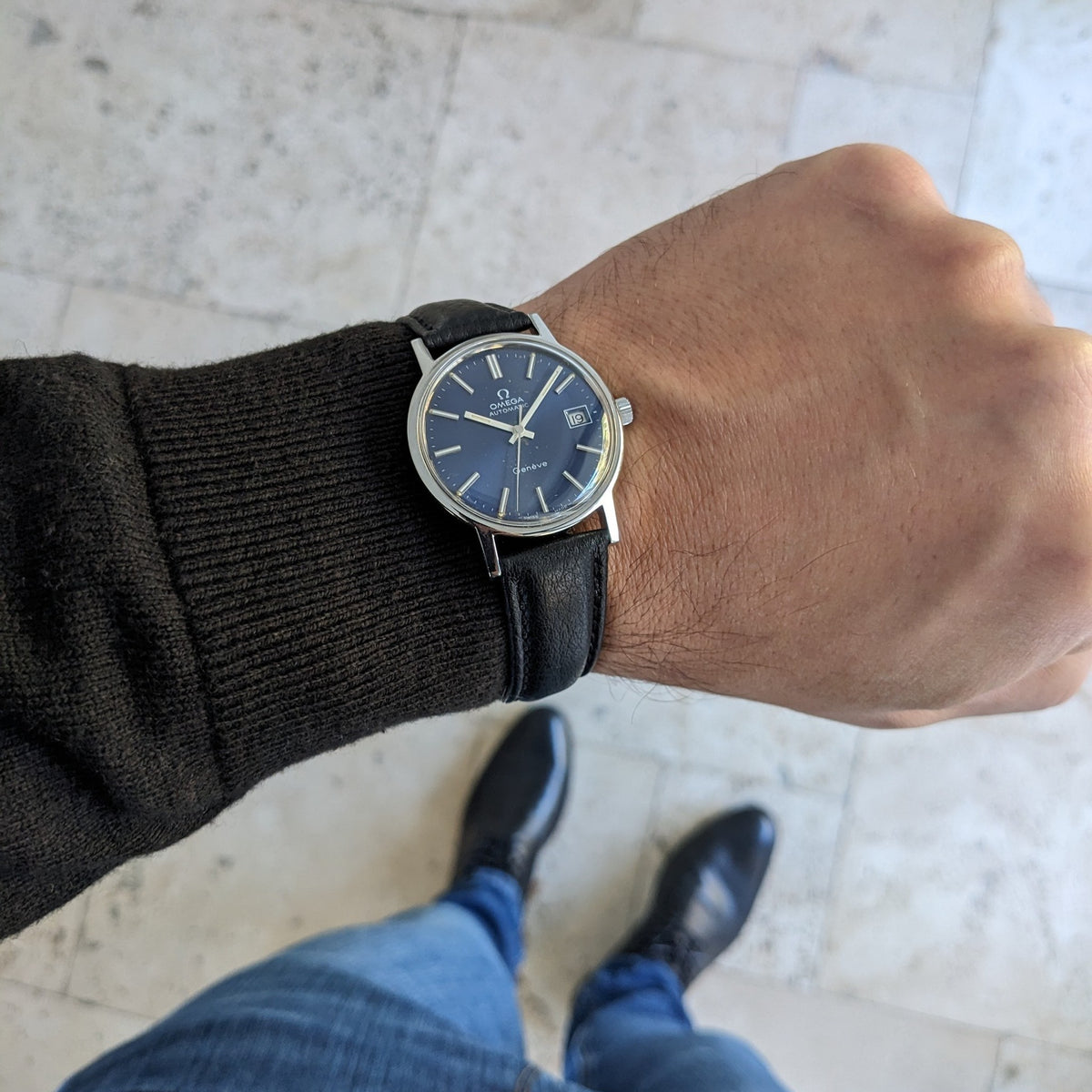 Omega Geneve Automatic reference 166.0163 worn on a wrist with a black leather strap, photographed against a pale tiled floor.