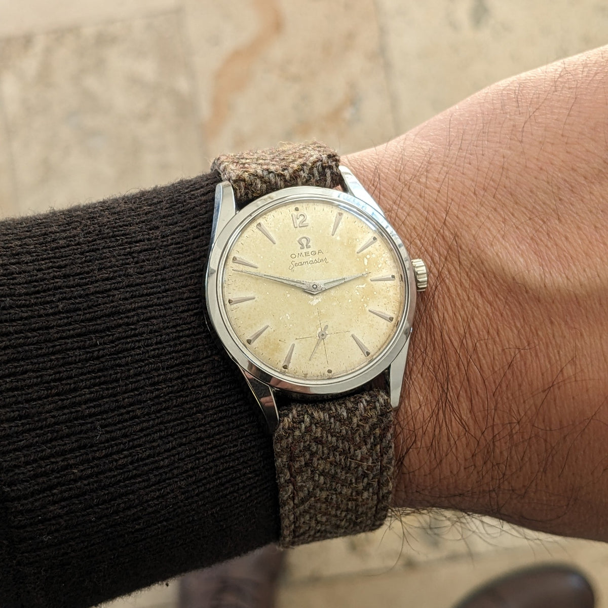 Omega Seamaster reference 29374 worn on a wrist, showing its cream dial, slim polished case, woven strap and black sleeve.