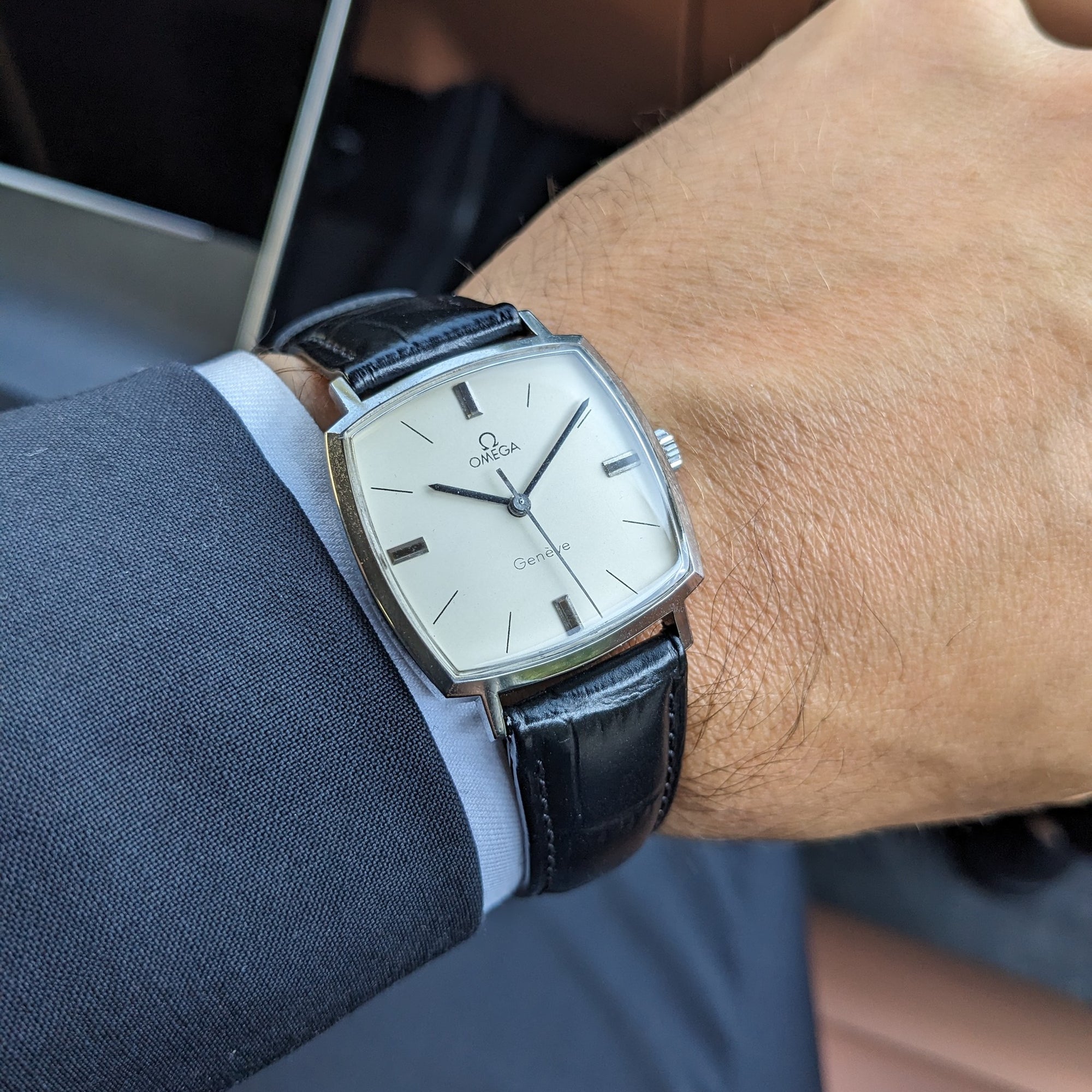 Omega Genève reference 131.022 worn on a wrist, showing the cream square dial, silver case, and black leather strap over a blue shirt cuff.