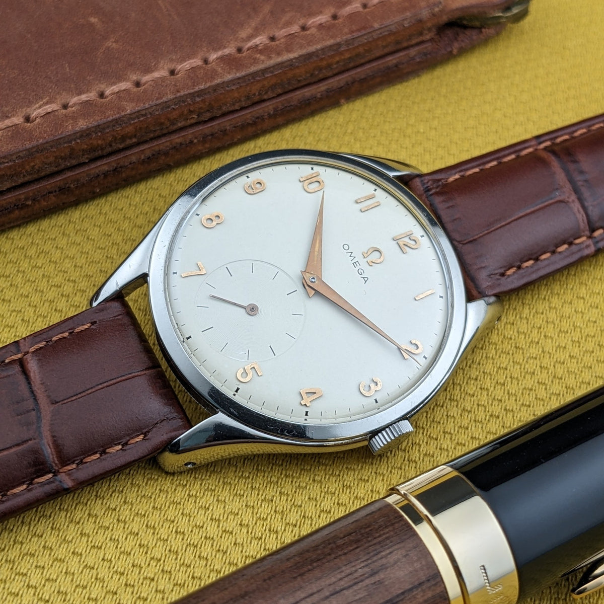Schrägansicht des Omega Jumbo Referenz 2505-10 Zifferblatts neben einem Holzstift und Lederportemonnaie, zeigt die kleine Sekunde.