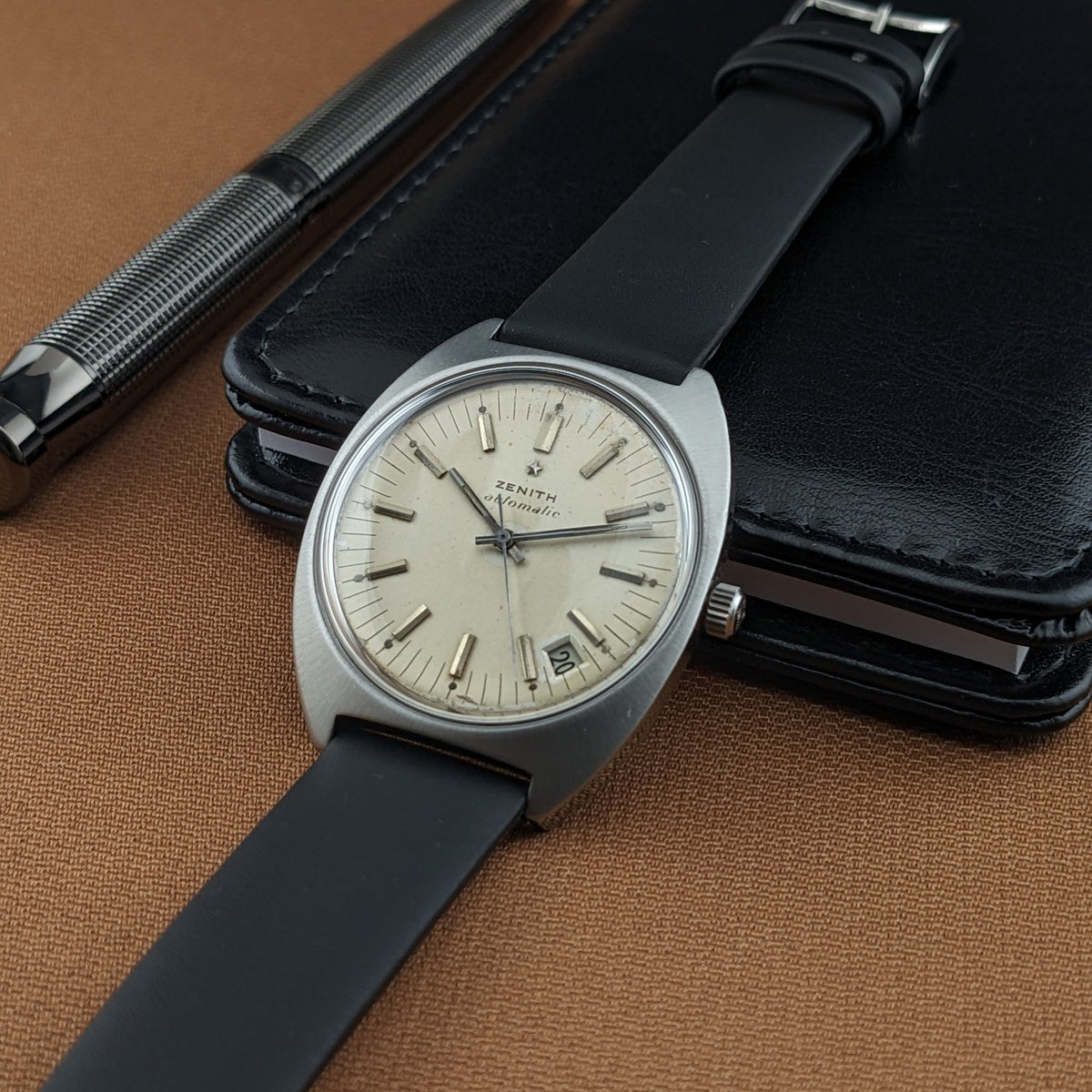 Angled Zenith Automatic reference GR 720001 resting on a black case, with its dial, crown, strap, and silver pen visible.