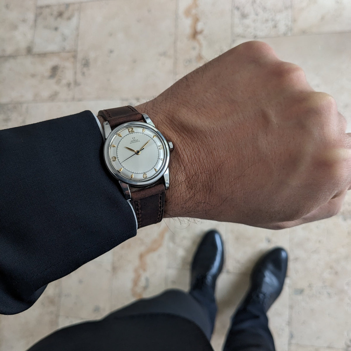 Omega Automatic Bumper reference 2767-4 SC shown on a wrist from above, with brown strap, cream dial and tiled floor background.