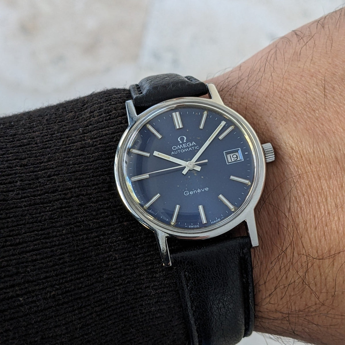 Close wrist view of the Omega Geneve Automatic reference 166.0163, showing its blue dial, date window, silver case and black strap.
