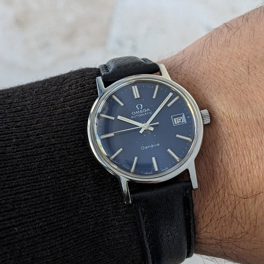 Close wrist view of the Omega Geneve Automatic reference 166.0163, showing its blue dial, date window, silver case and black strap.