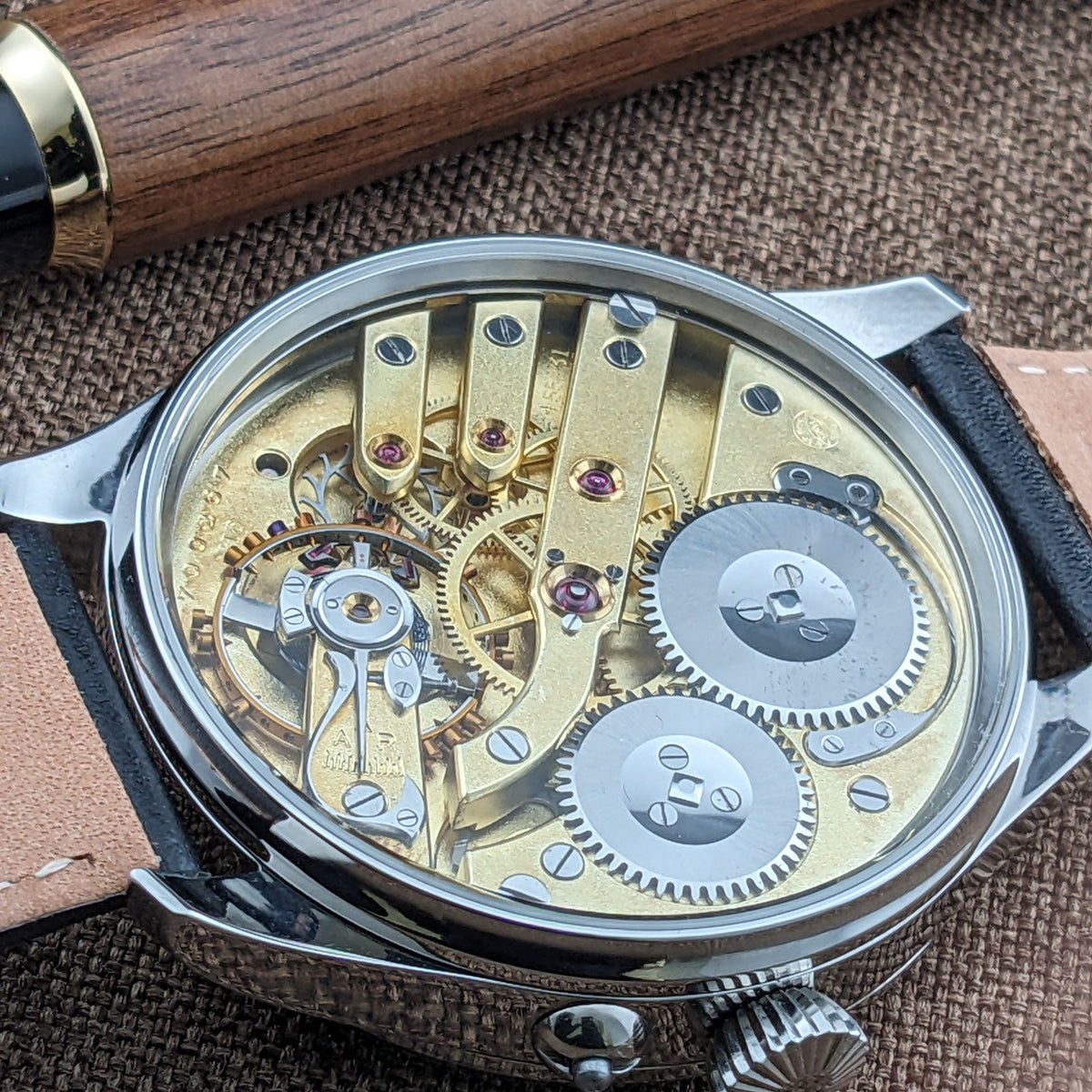 IWC Schaffhausen कलाई घड़ी का कोणीय पिछला दृश्य, पारदर्शी बैक, गिल्ट मूवमेंट, सिल्वर गियर्स, क्राउन और चमड़े की पट्टी दिखाता हुआ।