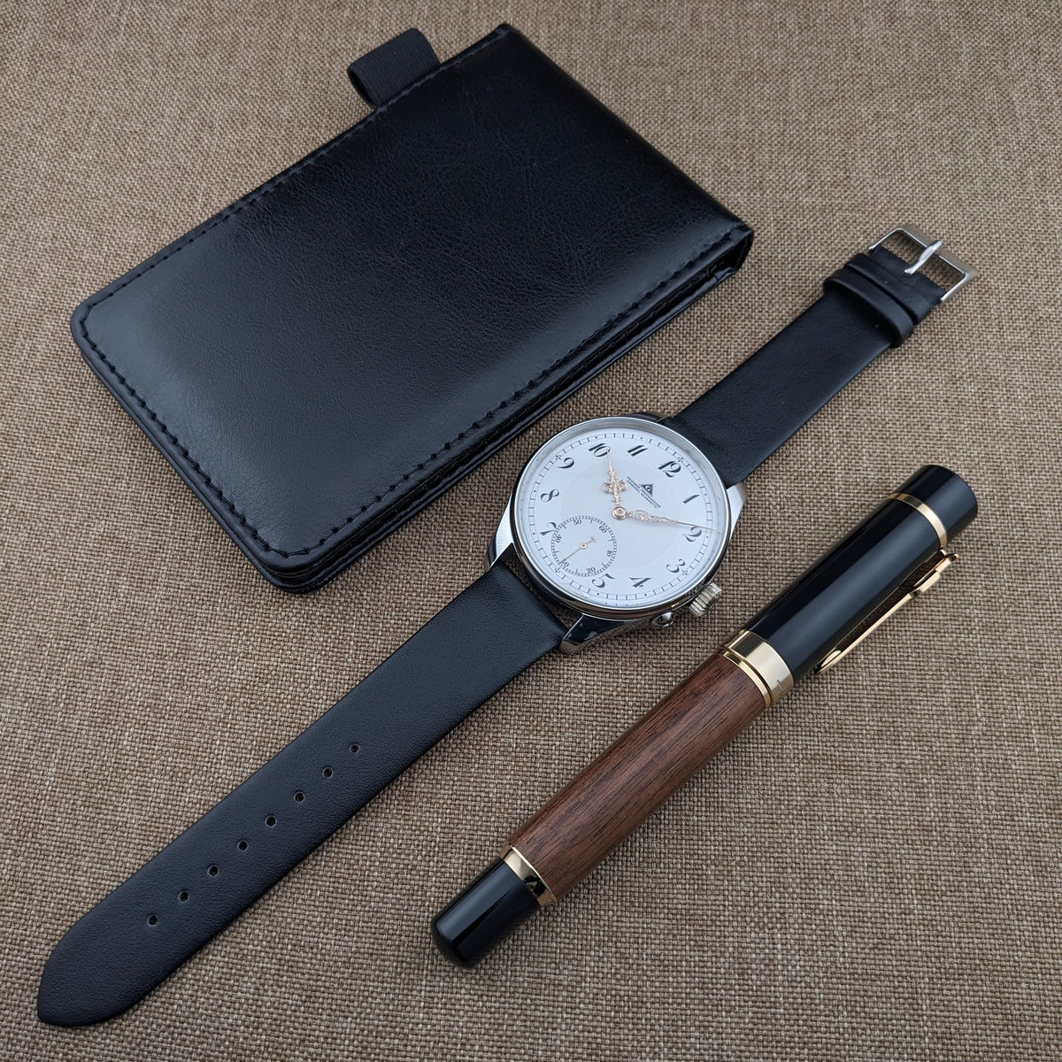 Deutsche Präzisionsuhr „Original Glashütte” mit schwarzem Armband neben einem schwarzen Etui und einem Holz-und-schwarz p