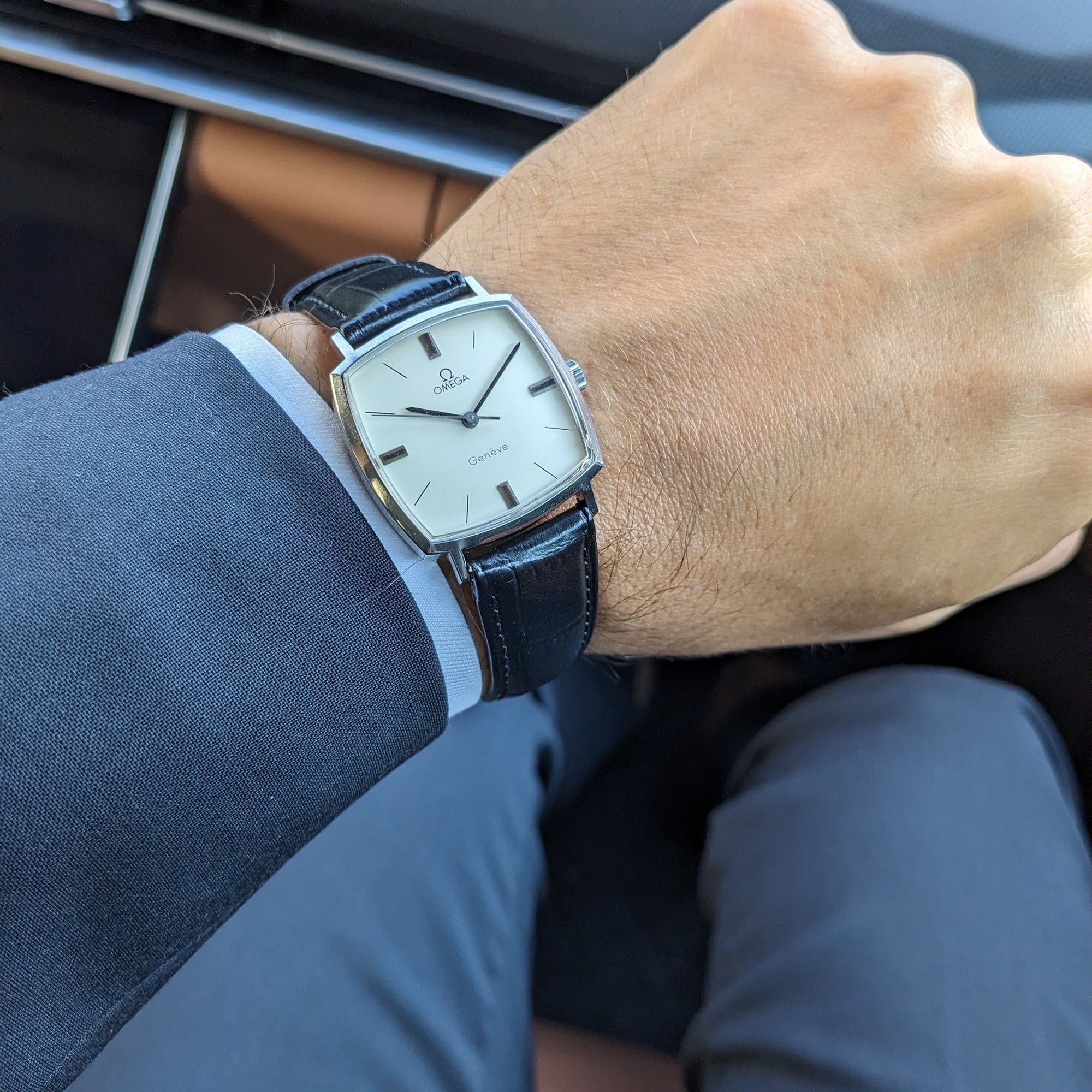 Omega Genève reference 131.022 pictured on a wrist inside a vehicle, with the cream dial and black leather strap visible.