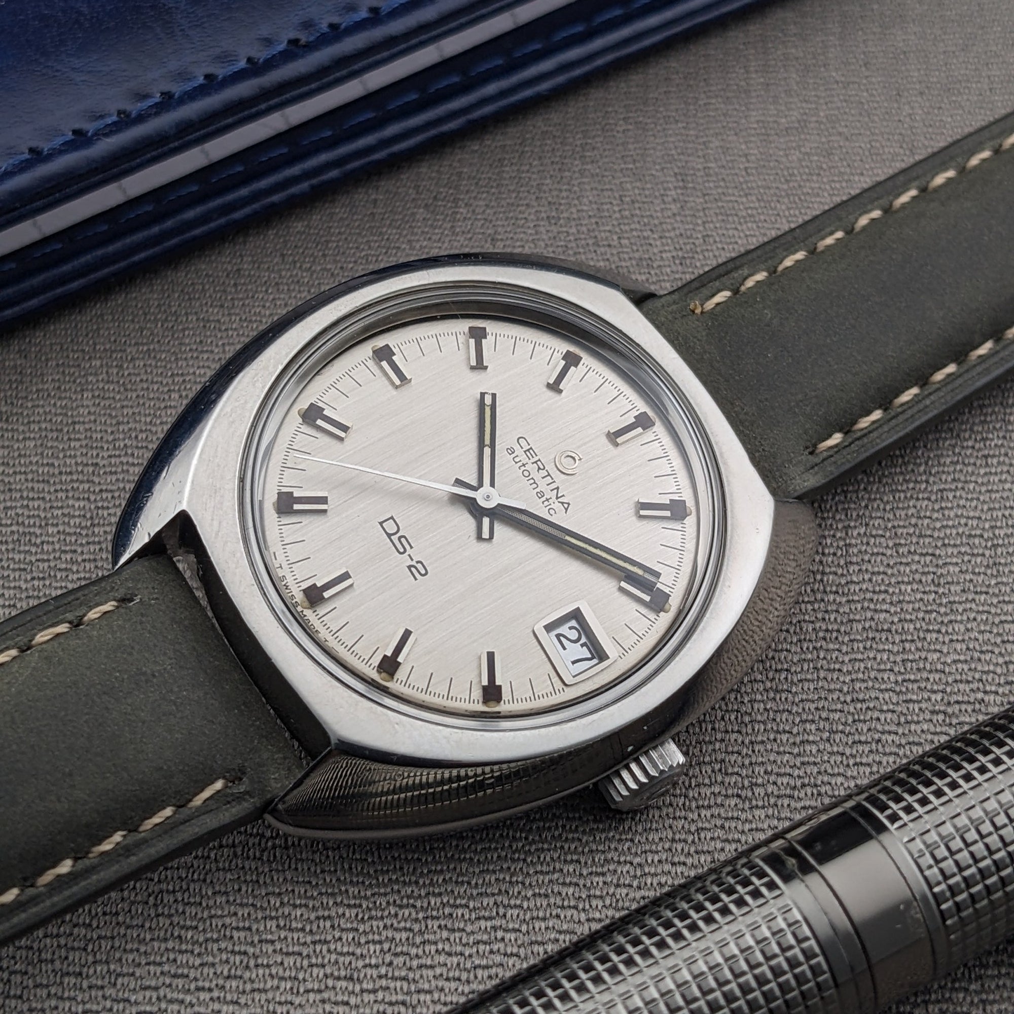 Certina DS-2 Automatic reference 5801 300 shown diagonally on textured fabric, with its silver dial, date window, crown, and stitched strap.