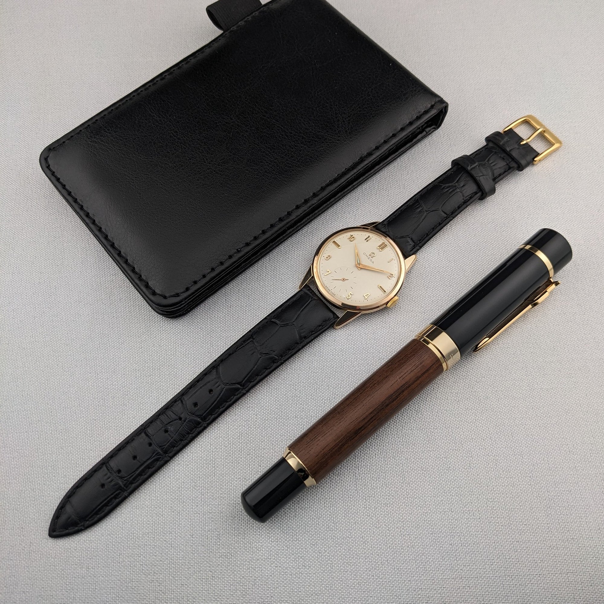 Omega Classic reference 14391-1 displayed with a black leather case and wooden-and-black pen, showing the full strap and gold-tone buckle.