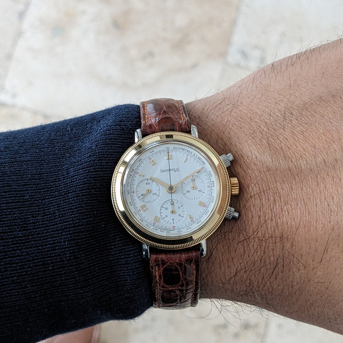 Eberhard & Co.. Godron Chrono reference 32031 worn on a wrist, with its white dial, gold-tone bezel and brown strap visible.