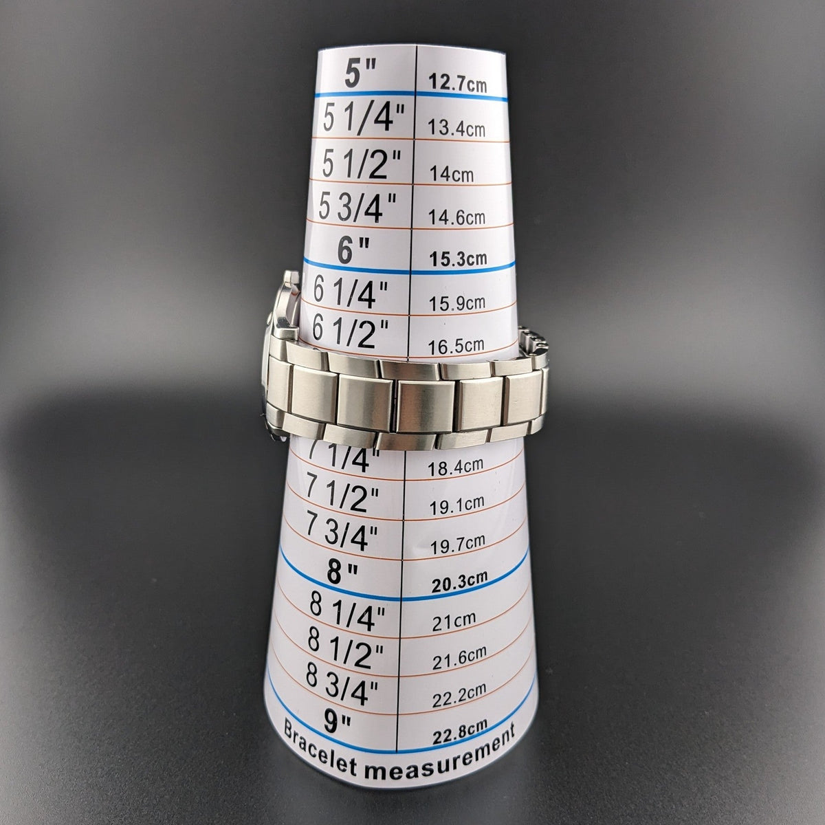 Bracelet de montre Movado enroulé autour d'un cône de mesure de bracelet marqué avec des étiquettes de taille en pouces et centimètres.