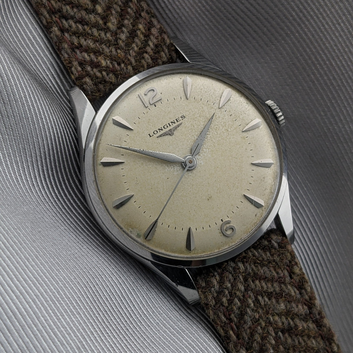 Angled close-up of the Longines Classic reference 8135-5 on gray fabric, highlighting its cream dial, silver hands and brown woven strap.