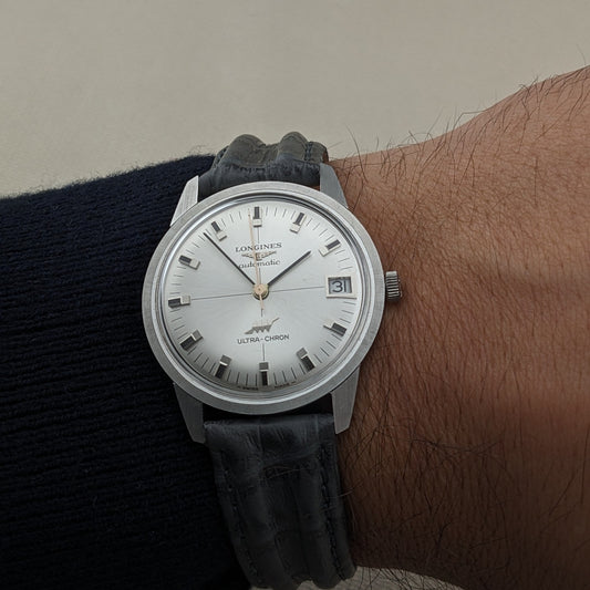 Close wrist view of the Longines Ultra-Chron 7827, with its silver dial, date window, crown, and black leather strap clearly visible.
