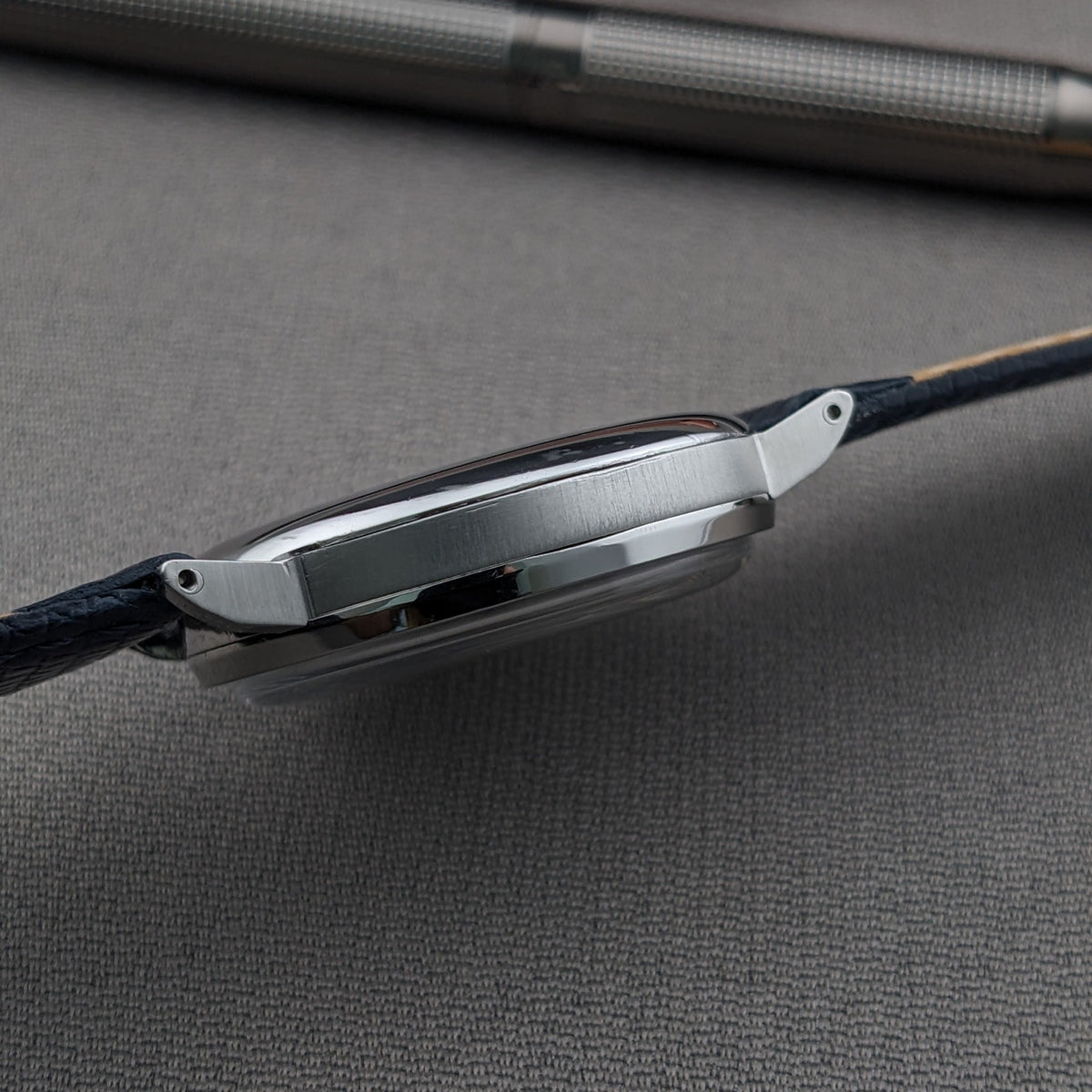Low side view of the Eberhard & Co. Pre-Extra Fort shows the slim round case, lugs, blue strap and textured pen above.
